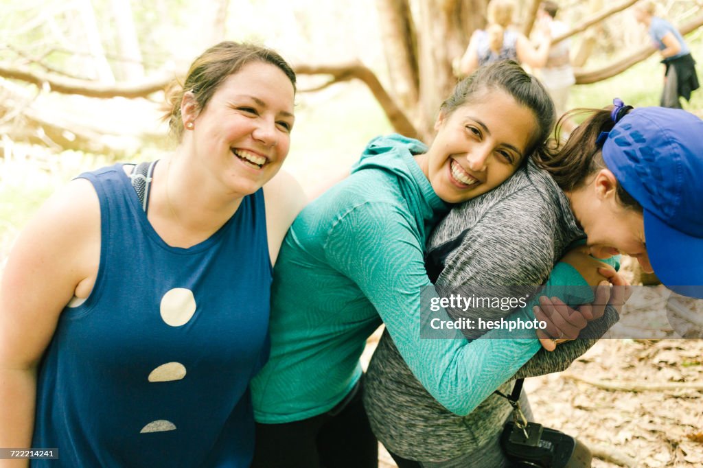 Three adult sisters hugging and laughing in forest, Maine, USA