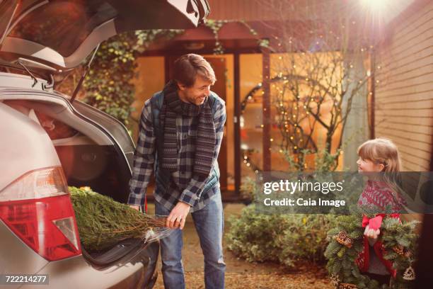 Father and daughter unloading Christmas tree from car outside house