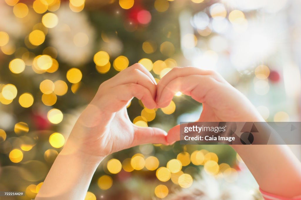 Close up hands of girl forming heart-shape in front of Christmas tree