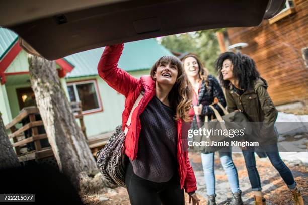 friends standing outside cabin, young woman closing boot of car - closing car boot fotografías e imágenes de stock