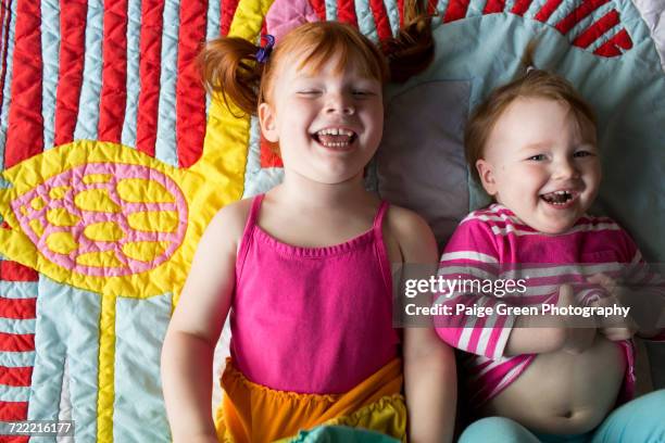 portrait of two young sisters lying on blanket, laughing - kids bright colour room stock pictures, royalty-free photos & images