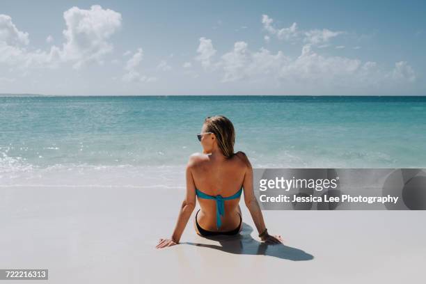 rear view of woman in bikini sitting on beach looking out at blue sea, anguilla, saint martin, caribbean - saint martin caraibi stock-fotos und bilder