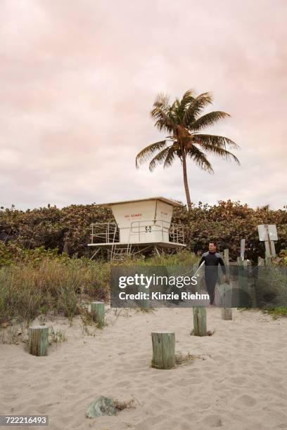 male lifeguard walking down beach with surfboard - stuart florida imagens e fotografias de stock