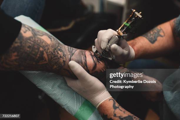 tattooist tattooing young mans arm, close-up - tatoeage stockfoto's en -beelden
