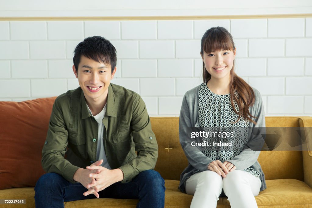 Portrait of young man and woman sitting on sofa