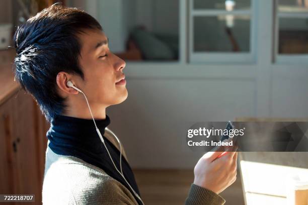 young man listening to music with mp3 player in room - music room stockfoto's en -beelden