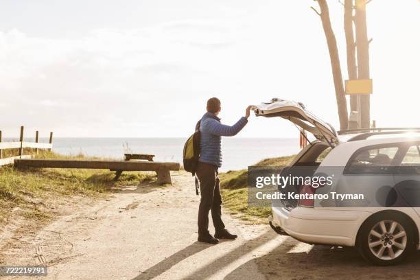 side view of man carrying backpack while standing by car on footpath - open rucksack stock pictures, royalty-free photos & images