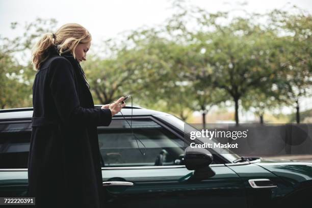 side view of businesswoman using mobile phone by car - car scandinavia stock pictures, royalty-free photos & images