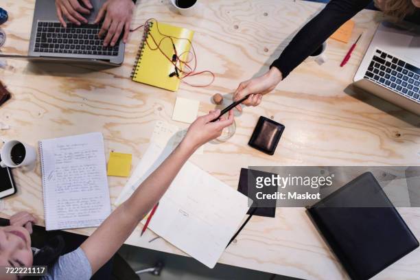 directly above shot of woman giving pen to colleague at wooden desk - arab businesswoman with books stock-fotos und bilder
