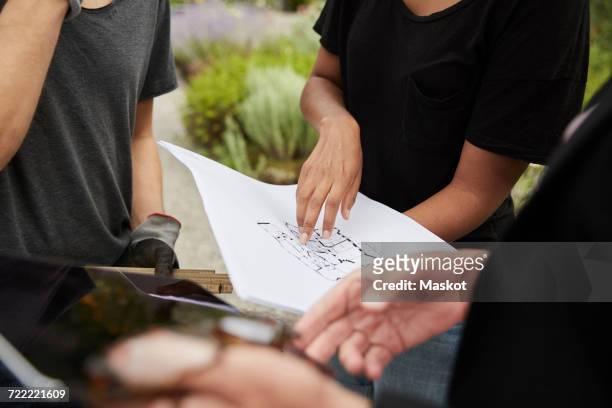 midsection of female garden architect explaining blueprint to colleagues - garden drawing stockfoto's en -beelden