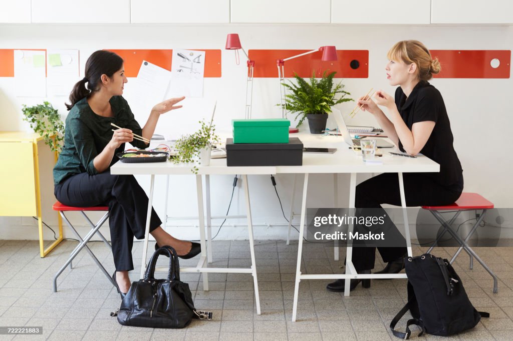 Full length of businesswomen talking while having lunch at table in office
