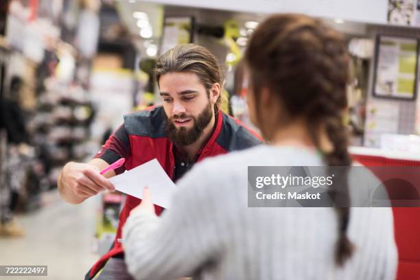 salesman giving document to female customer in hardware store - bouwmarkt stockfoto's en -beelden