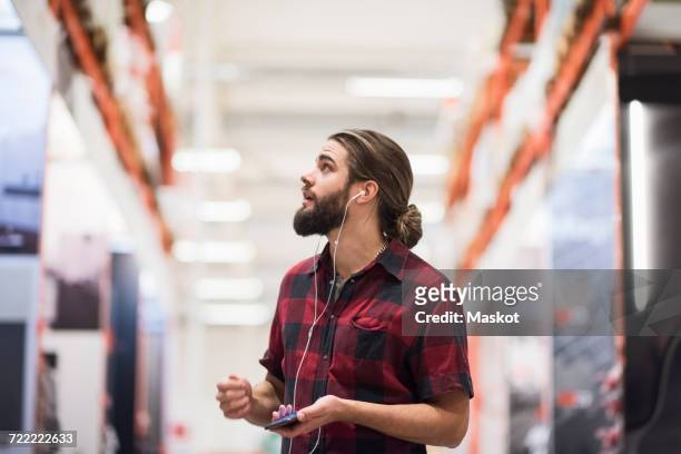customer looking up while listening music through smart phone at hardware store - magasin musique photos et images de collection