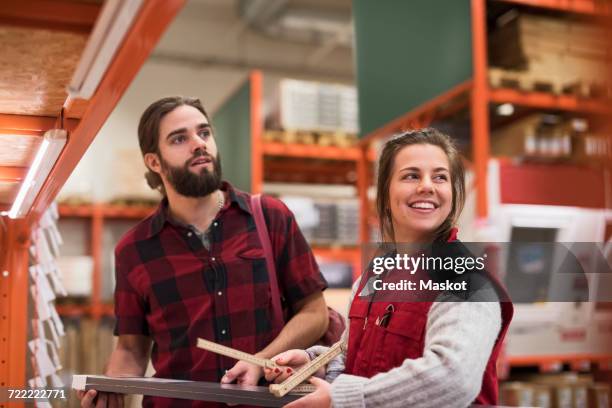 happy saleswoman looking away while standing with male customer in hardware store - sales assistant furniture stock pictures, royalty-free photos & images