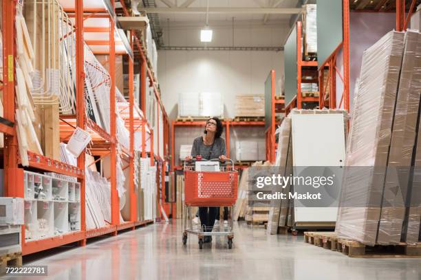 mature female customer looking up while pushing shopping cart in hardware store - ferramenta foto e immagini stock