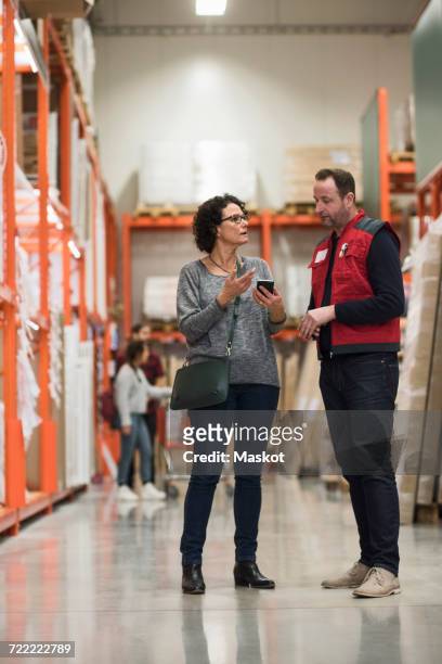 female customer talking to salesman while holding smart phone in hardware store - salesman photos et images de collection