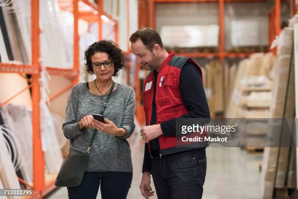 salesman and female customer using smart phone in hardware store - online guidance stock pictures, royalty-free photos & images
