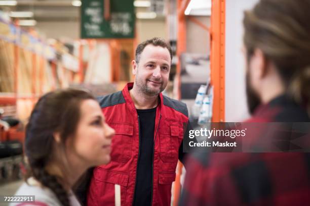 smiling salesman looking at couple in hardware store - shop seller photos et images de collection