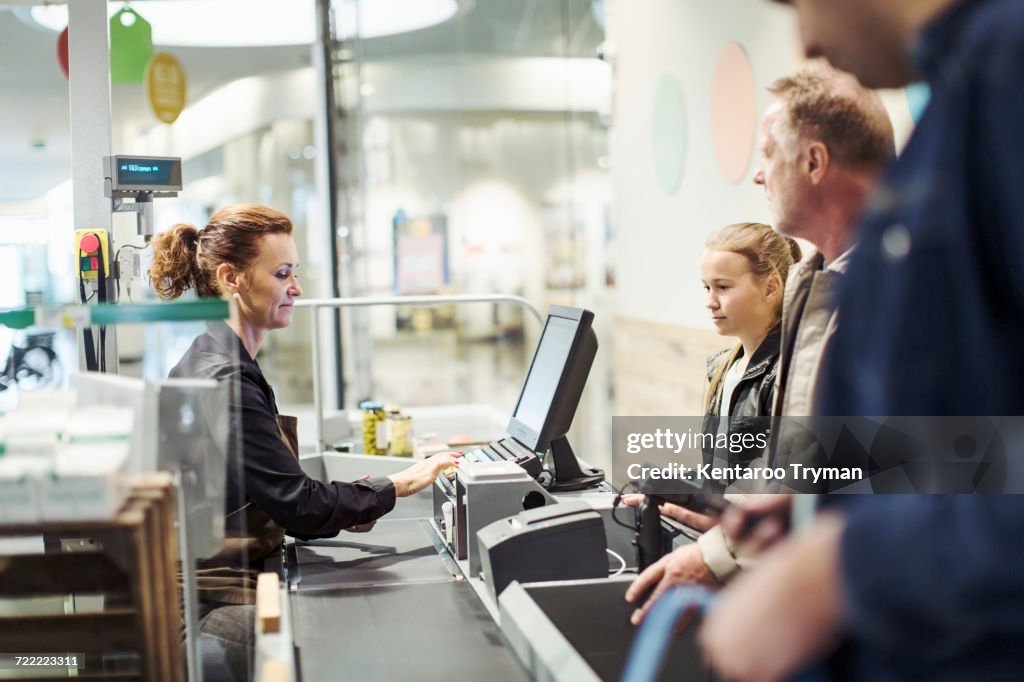 Side view of saleswoman using computer while customer standing at checkout counter in supermarket