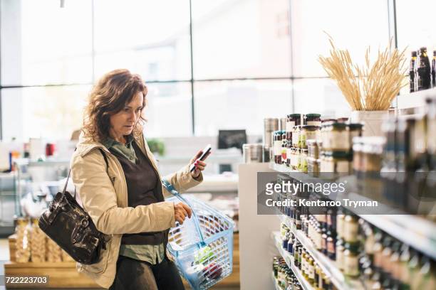 woman holding smart phone while shopping in supermarket - female supermarket foto e immagini stock