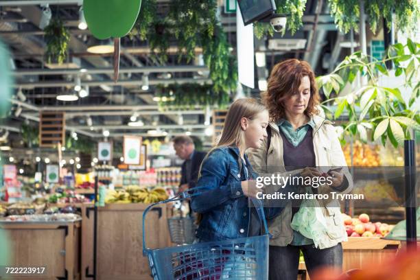 mother and daughter using smart phone in organic foodstore - supermercado fotografías e imágenes de stock