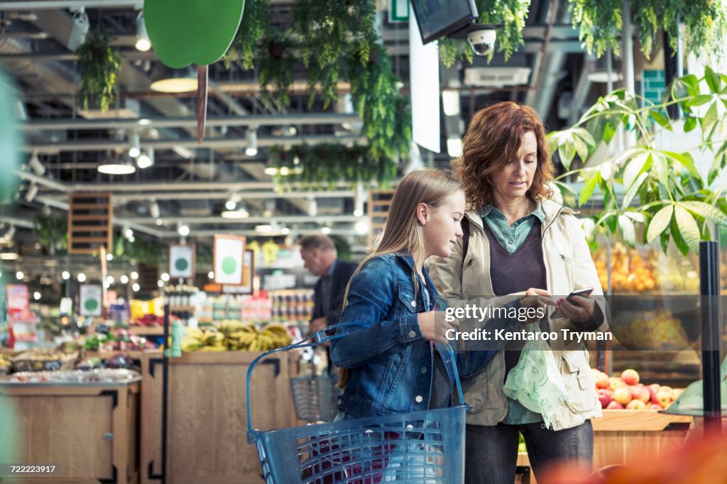 Mother and daughter using smart phone in organic foodstore
