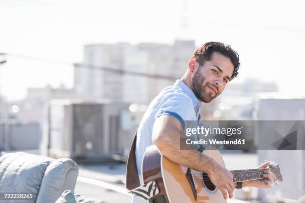 young man on rooftop sitting on sofa and playing guitar - male musician stock pictures, royalty-free photos & images