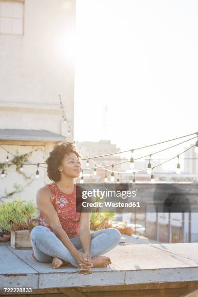 young woman sitting on rooftop terrace, enjoying the sun - dachterasse stock-fotos und bilder