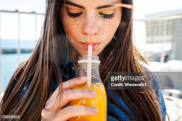 young woman with freckles drinking orange juice - orange juice stock-fotos und bilder