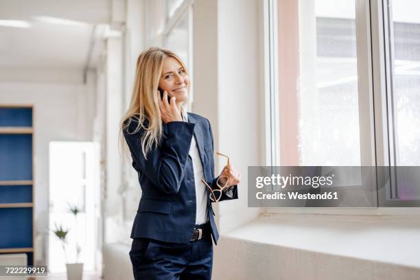 portrait of smiling businesswoman on cell phone in office - blonde business woman stock-fotos und bilder