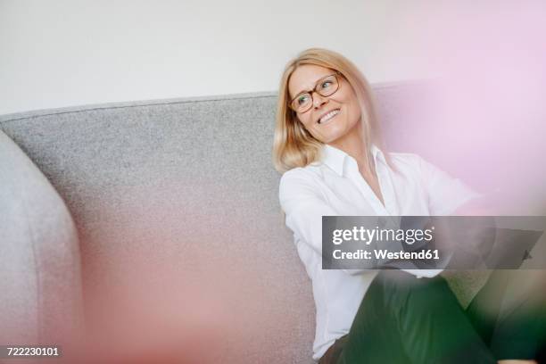 smiling relaxed businesswoman sitting on couch - casual woman business stock-fotos und bilder