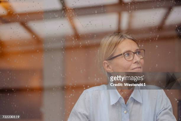 businesswoman behind rainy windowpane looking away - window rain stock-fotos und bilder