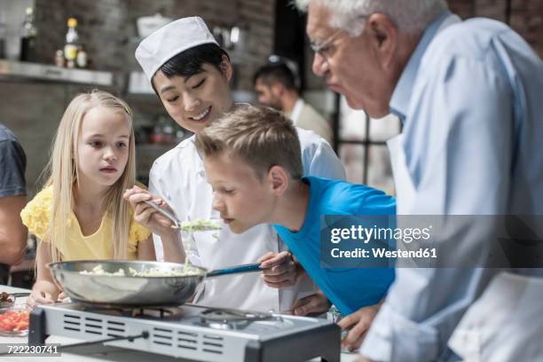 female chef letting child smell from frying pan - children cooking school stock pictures, royalty-free photos & images