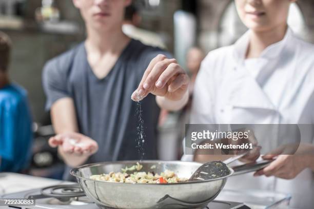 teenager adding salt to pan - uniforme de cozinheiro - fotografias e filmes do acervo