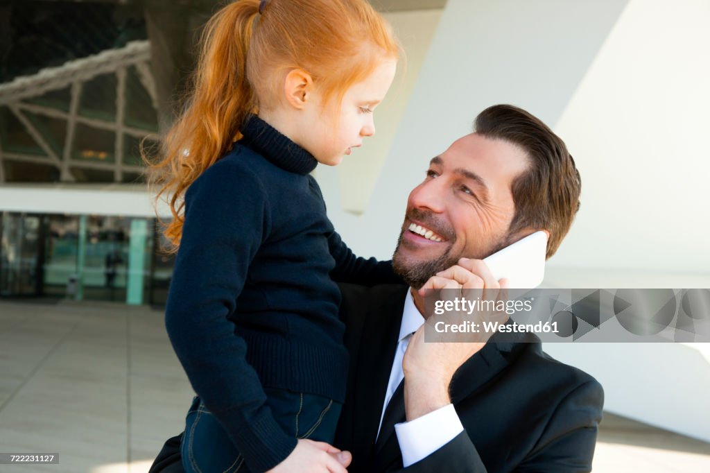 Smiling businessman on the phone holding daughter