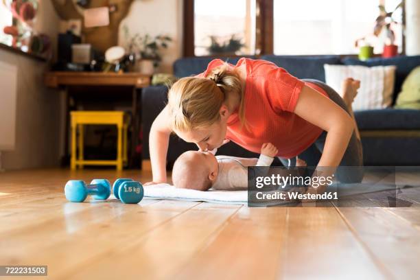 happy mother kissing baby at home lying on mat next to dumbbells - hand weight stock pictures, royalty-free photos & images