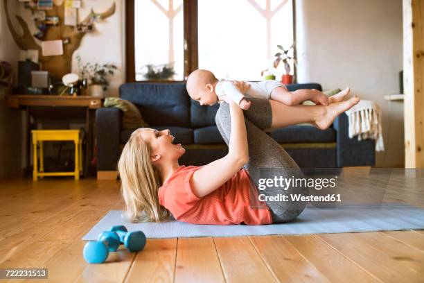 happy mother lifting up baby at home lying on mat - eltern baby hochheben stock-fotos und bilder