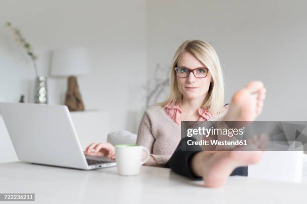 portrait of blond woman at home sitting at table with feet up - female soles stock-fotos und bilder