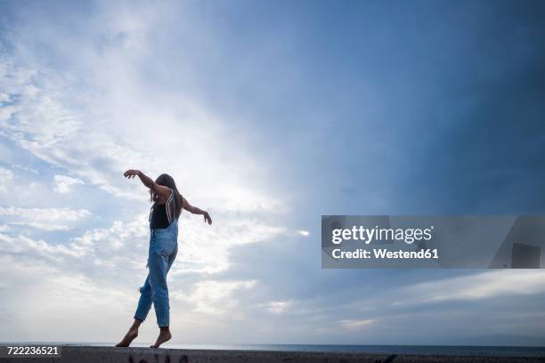 woman with arms outstretched balancing on wall in front of sky - balance stock pictures, royalty-free photos & images