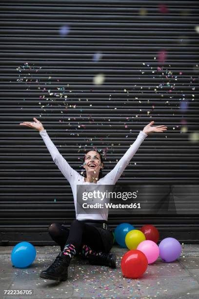 happy young woman sitting on pavement with balloon throwing confetti - balloon woman party stock pictures, royalty-free photos & images