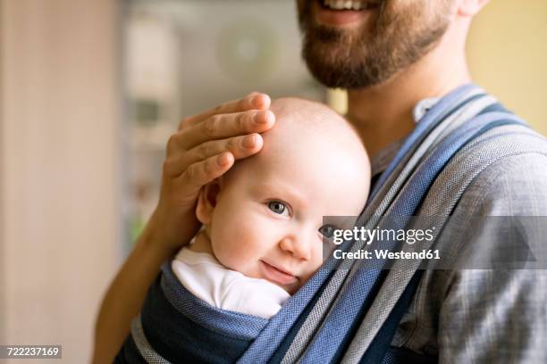 father with baby son in sling at home - portabebés fotografías e imágenes de stock