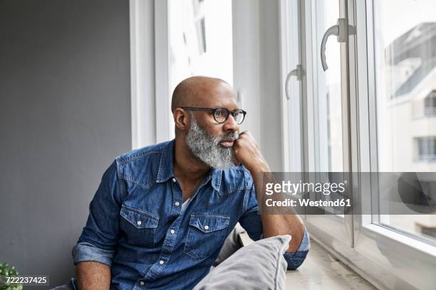 mature man sitting at window, looking worried - hand am kinn stock-fotos und bilder