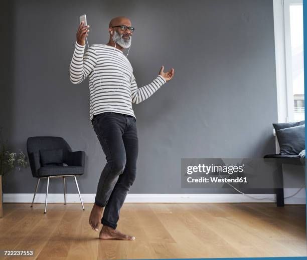 mature man dancing alone at home, holding smart phone - man dancing - fotografias e filmes do acervo