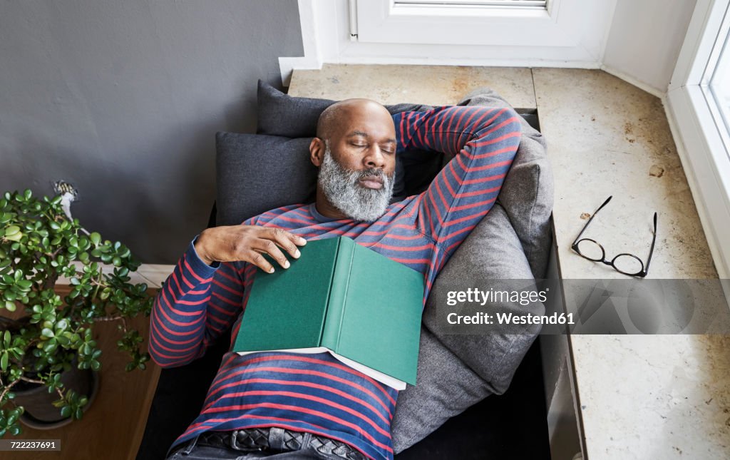 Matur man lying on bench with a book, taking a nap