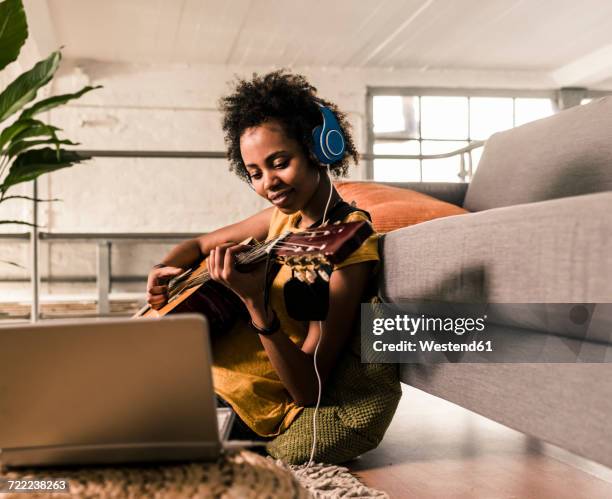 young woman at home with headphones and laptop playing guitar - learn guitar stockfoto's en -beelden