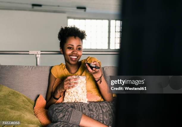 laughing young woman sitting on couch watching tv - watching tv sofa stock-fotos und bilder