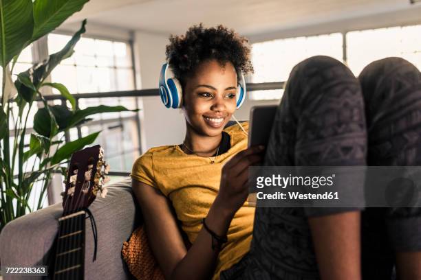 smiling young woman on couch with headphones using tablet - arts culture and entertainment stock-fotos und bilder