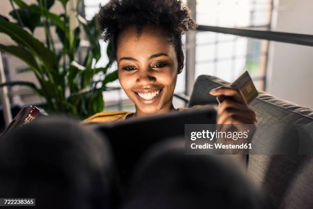 smiling young woman on couch with credit card and laptop - compras em casa imagens e fotografias de stock