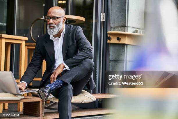 mature businessman sitting in cafe using laptop - bald man stockfoto's en -beelden