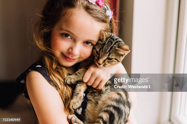 portrait of little girl holding tabby kitten - girls cuddling cat stock-fotos und bilder